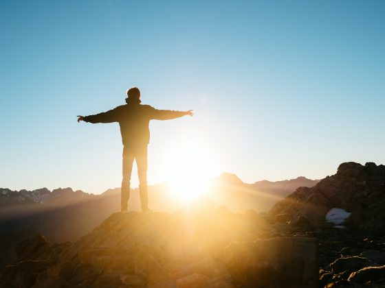 seseorang berdiri merentangkan tangan di atas gunung menghadap matahari