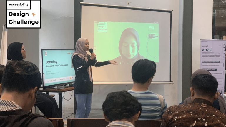 Foto suasana sebuah ruangan yang berisi sekumpulan orang duduk dan menghadiri event. Tampak seorang perempuan berhijab, mengenakan mic di depan audiens yang duduk, dengan membelakangi sebuah tv bertuliskan Demoday Accessibility design challenge, dan layar yang terdapat seorang perempuan bersiap untuk presentasi.